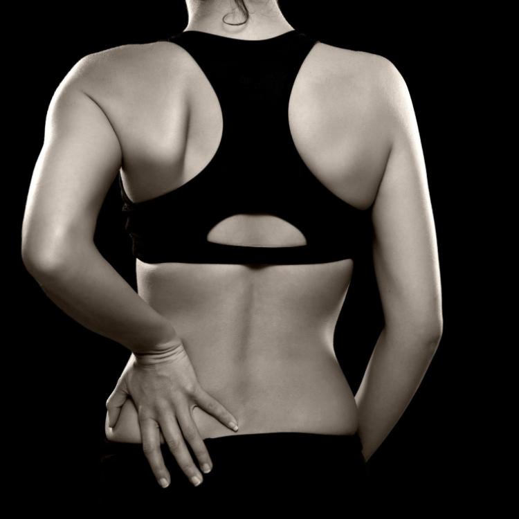 20494423 - a black and white photo of an athletic woman holding her lower back as if experiencing pain
