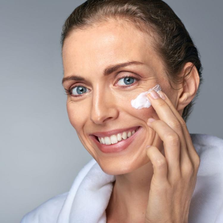 56782540 - portrait of beautiful radiant mature woman applying some cream to her face, skin care cosmetics wellness concept