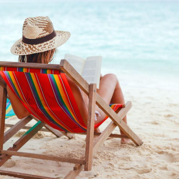 17444511 - young beautiful woman sitting on beach reading a book