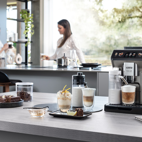 Na pierwszym planie automatyczny ekspres do kawy Eletta Explore De’Longhi, a w tle dwie młode kobiety pijące kawę. (Fot. materiały partnera)