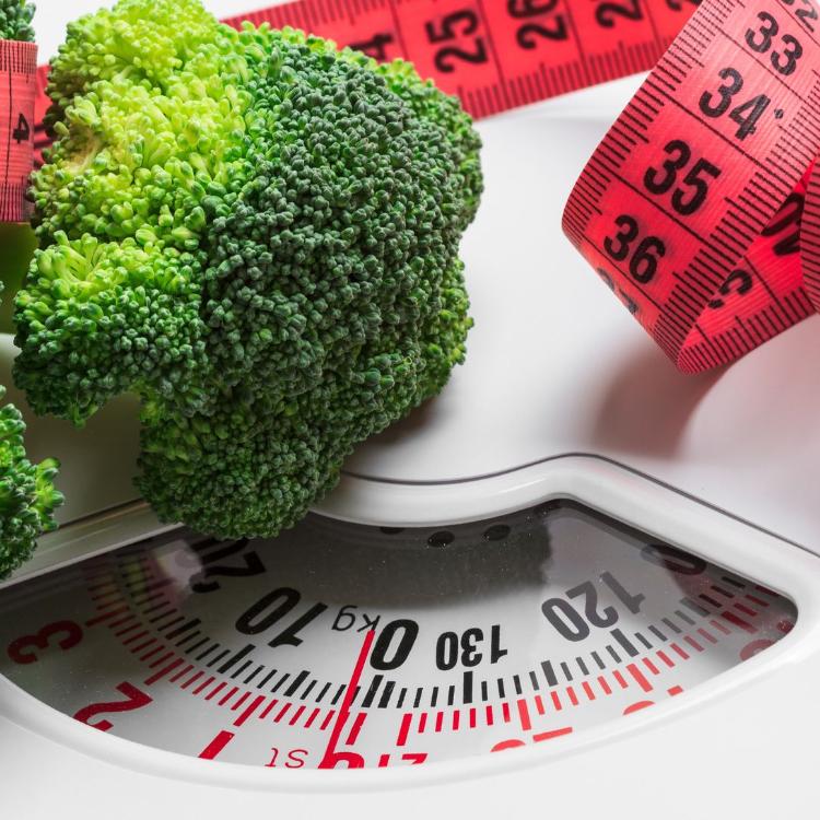 Dieting healthy eating slim down weight control concept. Closeup green broccoli with measuring tape on white scales