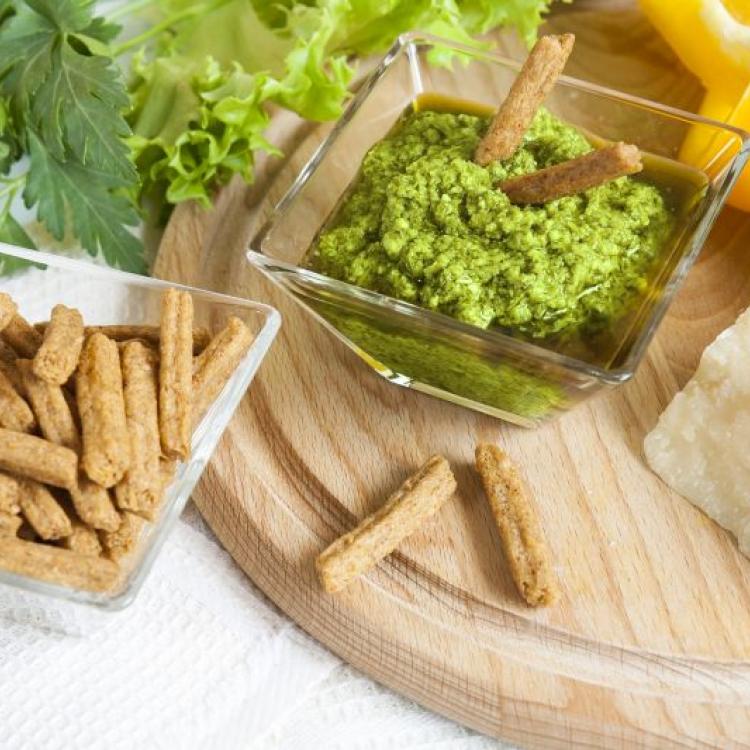 Basil pesto with bread rusks parmigiano cheese fresh yellow pepper lettuce leaves parsley on wooden board and napkin background