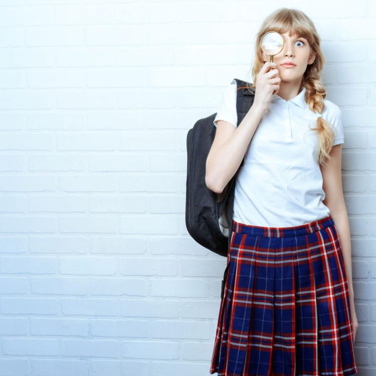 42782967 - cute teen girl in school uniform looking through a magnifying glass. education. studio shot.