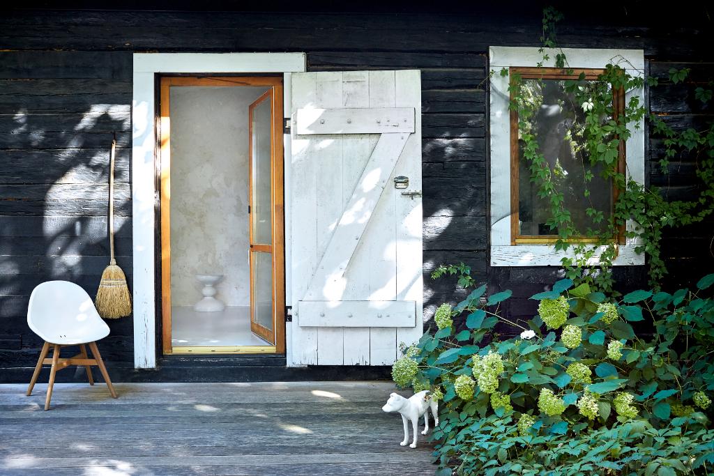 Ponadstuletnie drewniane belki naturalnie sczerniały. Fasadę budynku rozjaśniają białe drzwi i szerokie obramowania okien. Latem życie domowników toczy się na tarasie i w ogrodzie. (Fot. Celestyna Król)