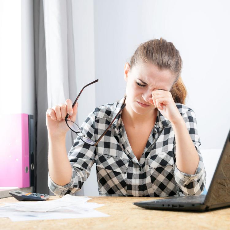 62261963 - tired young woman with eye pain during working in home office using laptop