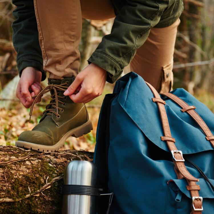 33853055 - female hiker tying shoelaces outdoors in autumn forest, near thermos and backpack. view of legs. hiking and leisure theme