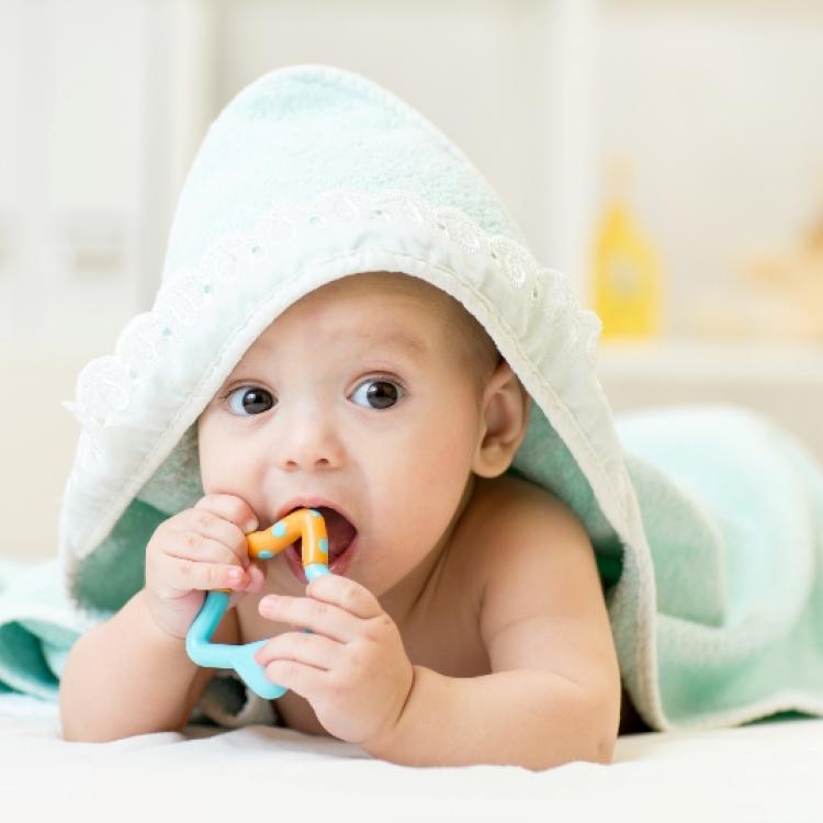 baby with teether in mouth under bathing towel at nursery