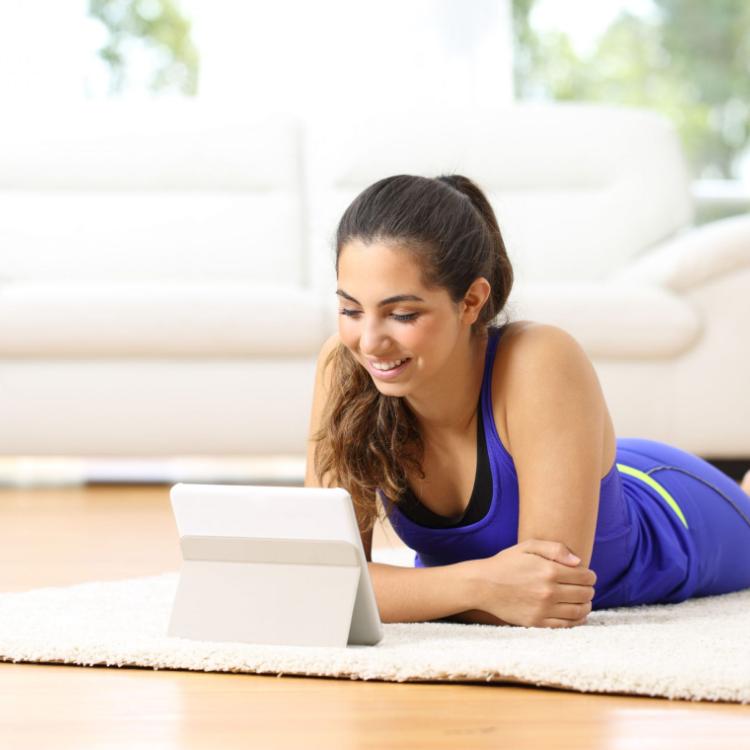 50573139 - sportswoman watching sport videos in a tablet lying on the floor at home