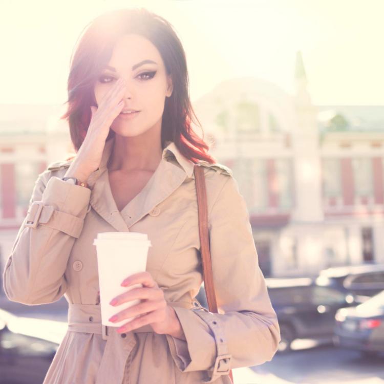 41237201 - beautiful young woman in a modern trench coat, holding a disposable takeaway cup and standing against urban city background.