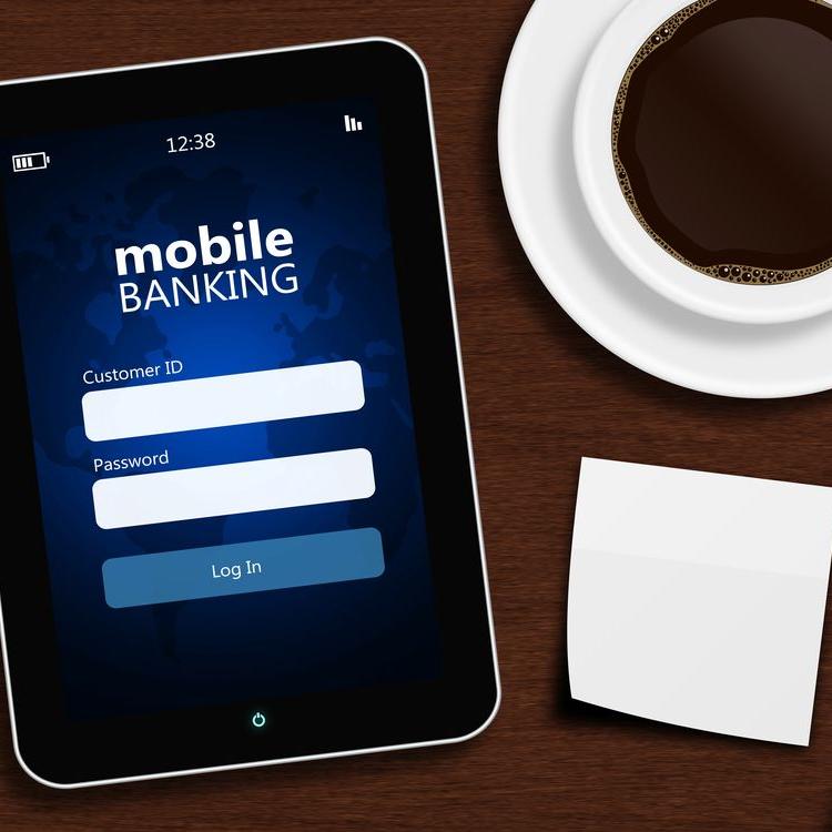 tablet with mobile banking login page, cup of coffee, pen and white note lying on wooden desk
