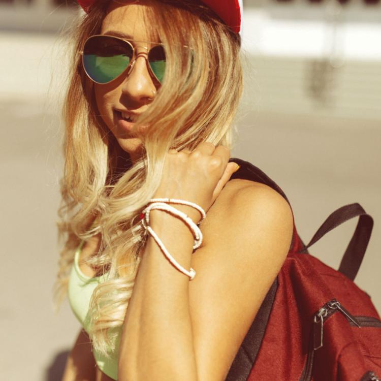 48757271 - sexy blonde young woman wearing sunglasses, shorts, cap, green top and backpack walking on the street. camera film effect