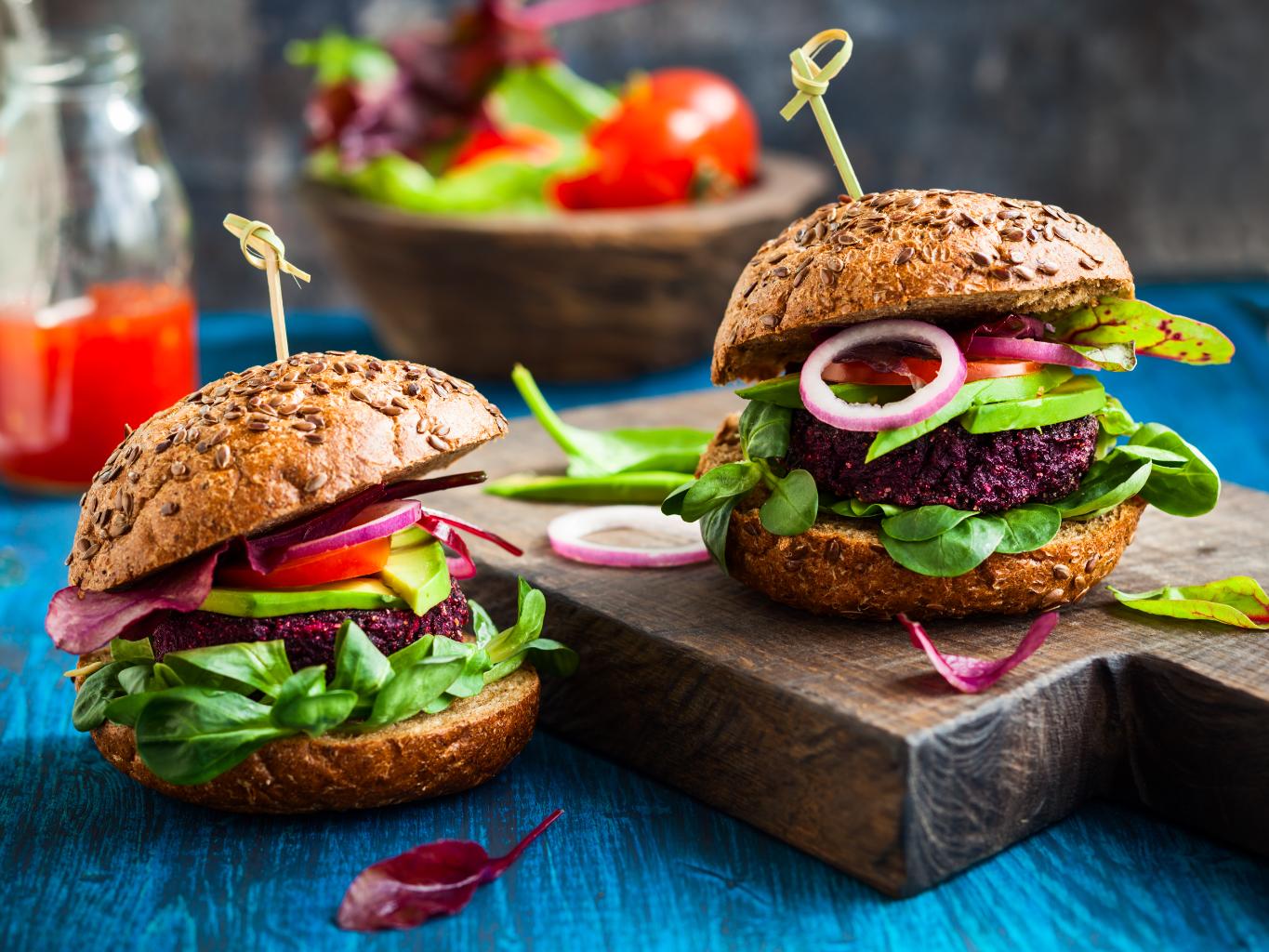 Dwa wegańskie burgery z buraka z warzywami i w bułce, leżące na drewnianej desce (Fot. materiały partnera)